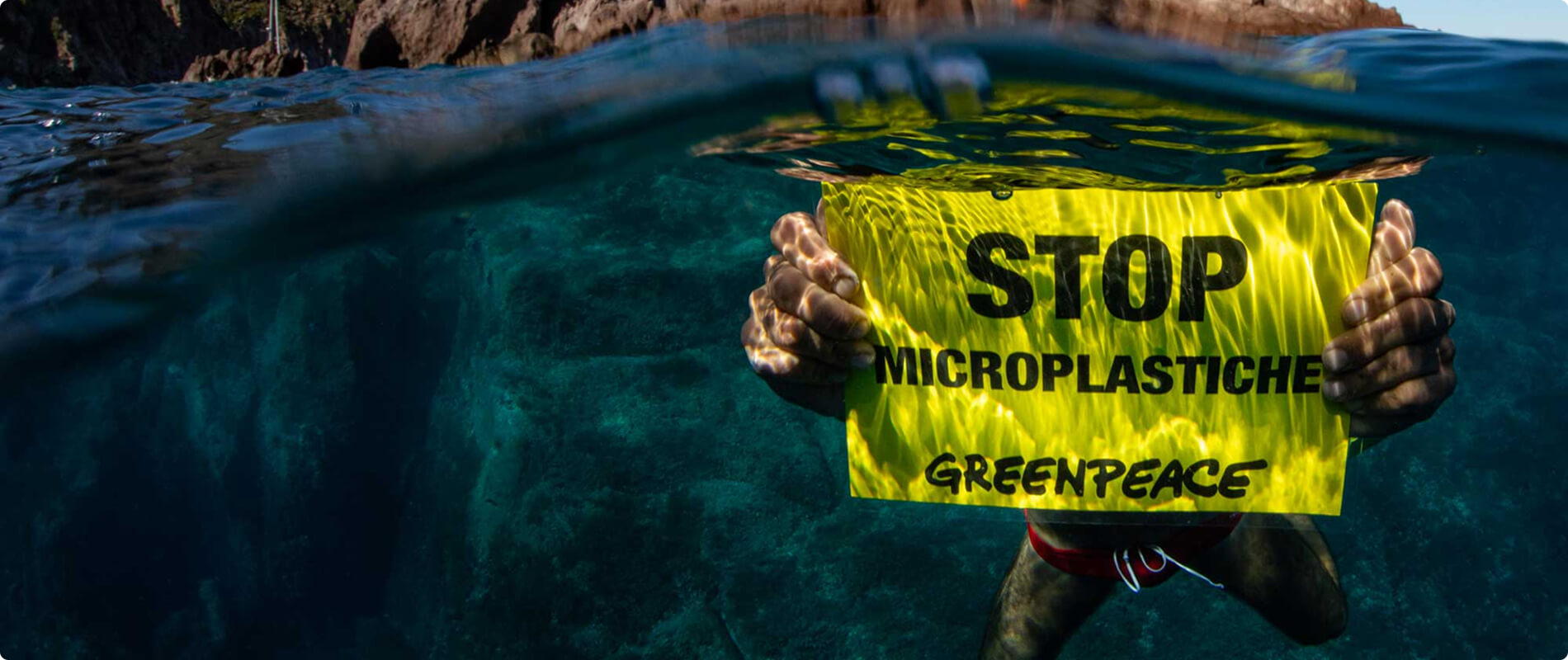 Attivista in acqua con un cartello Greenpeace contro le microplastiche.